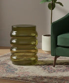 Green glass side table next to a green armchair in a living room setting.