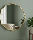 Decorative wall mirror with a gold frame on a green wall, next to a plant and a tufted chair.