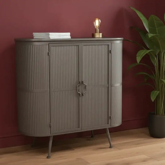 Gray cabinet with books and a lamp against a red wall with a plant on the right.