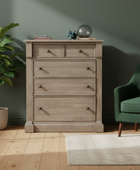 Wooden dresser with decorative items in a room with a green wall, plant, and green sofa.