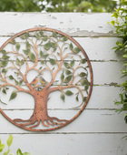 Decorative metal tree wall art on a white wooden fence with greenery.