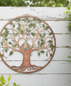 Decorative metal tree wall art on a white wooden background with greenery.