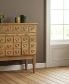 Wooden dresser with card catalog design in a room with a window and plant.