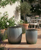 Two gray planters on a patio with garden and table in the background
