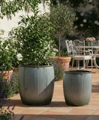 Two gray planters with green plants on a patio with outdoor furniture in the background.