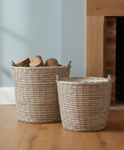 Two wicker baskets with firewood on a wooden floor in front of a fireplace.