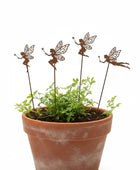 Terracotta pot with green plants and four decorative fairy stakes on a white background