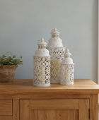 Three decorative lanterns on a wooden surface with a plant in the background