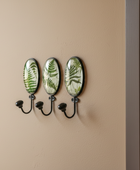 Wall hook with three decorative plates featuring leaf patterns on a beige wall.