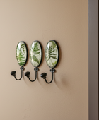 Wall-mounted hook with three decorative plates featuring fern designs on a beige wall.