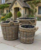 Three wicker planters with black liners on a stone patio in front of a house.