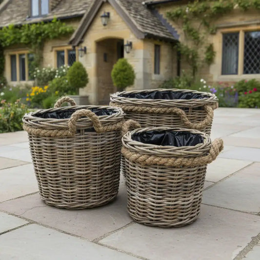 Three wicker planters with black liners on a stone patio in front of a house.