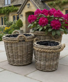 Wicker planters with pink flowers on a stone patio in front of a house.