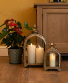 Decorative lanterns with candles on a wooden floor next to a potted plant and wooden cabinet.