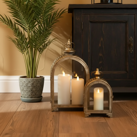 Decorative lanterns with candles on a wooden floor next to a plant and dark wooden cabinet.