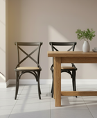 Dining table with two chairs in a room with a neutral wall and tiled floor.