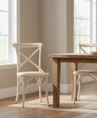 Wooden dining table with two chairs in a bright room with large windows.