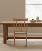 Wooden dining table with chair in a room with large windows.