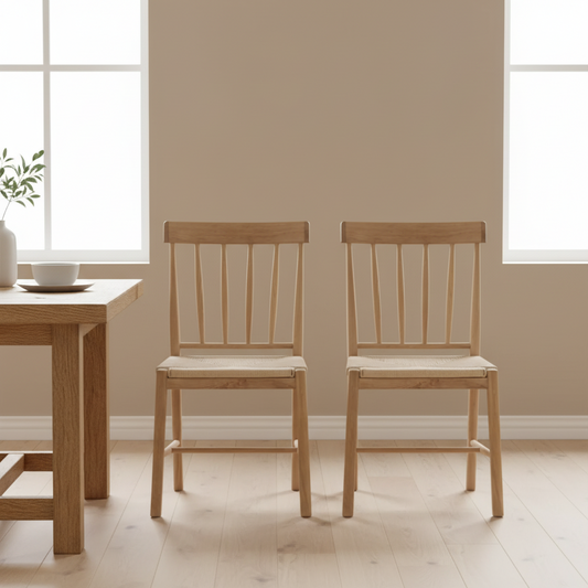 Two wooden chairs in a room with a table and windows.