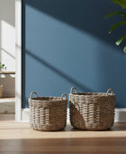 Two wicker baskets on a wooden floor with a blue wall in the background
