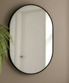 Round mirror with black frame on a beige wall next to a green plant