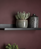 Black shelf with a potted plant and a black and white vase against a purple wall