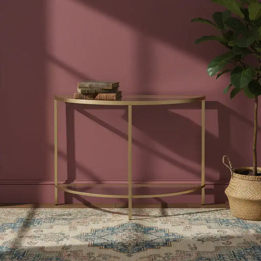 Gold console table against a pink wall with a plant and books on it