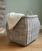 Wicker laundry basket with a white towel on a wooden floor against a stone wall.