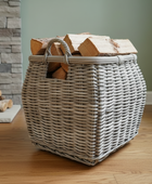 Wicker basket with firewood on a wooden floor against a stone wall.