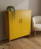 Yellow cabinet with gold handles next to a beige chair on a wooden floor.
